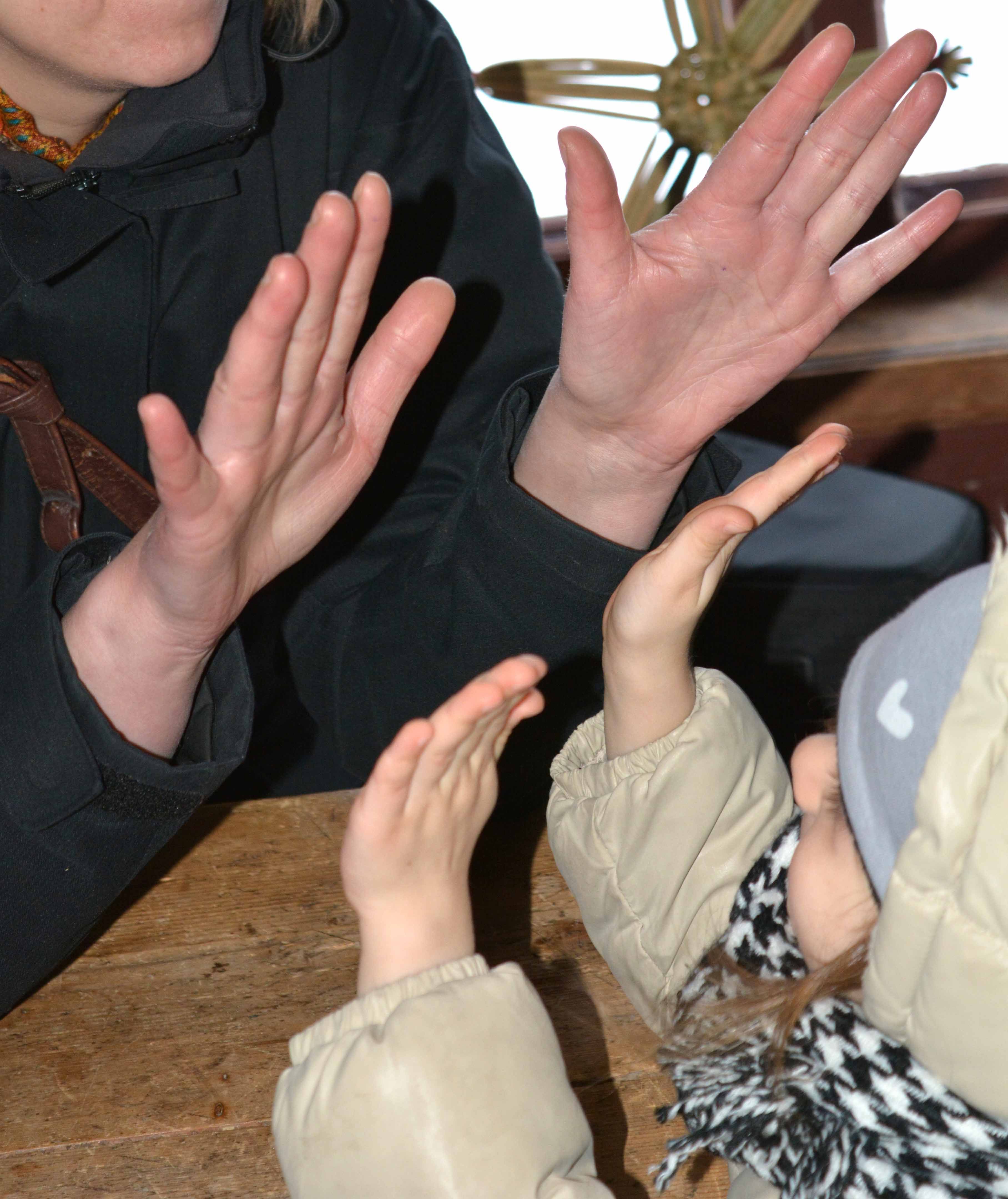 Bolden visar en flicka och en vuxen, som håller upp händerna mot varandra i en klapplek. De sitter vid ett bord och bilden är beskuren för att fokucera på deras händer. 